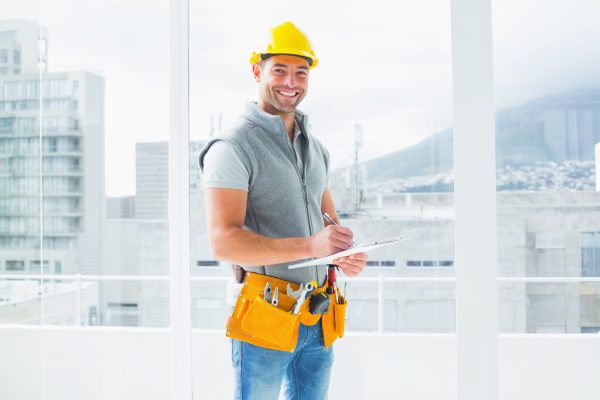 Portrait of smiling manual worker writing on clipboard in building